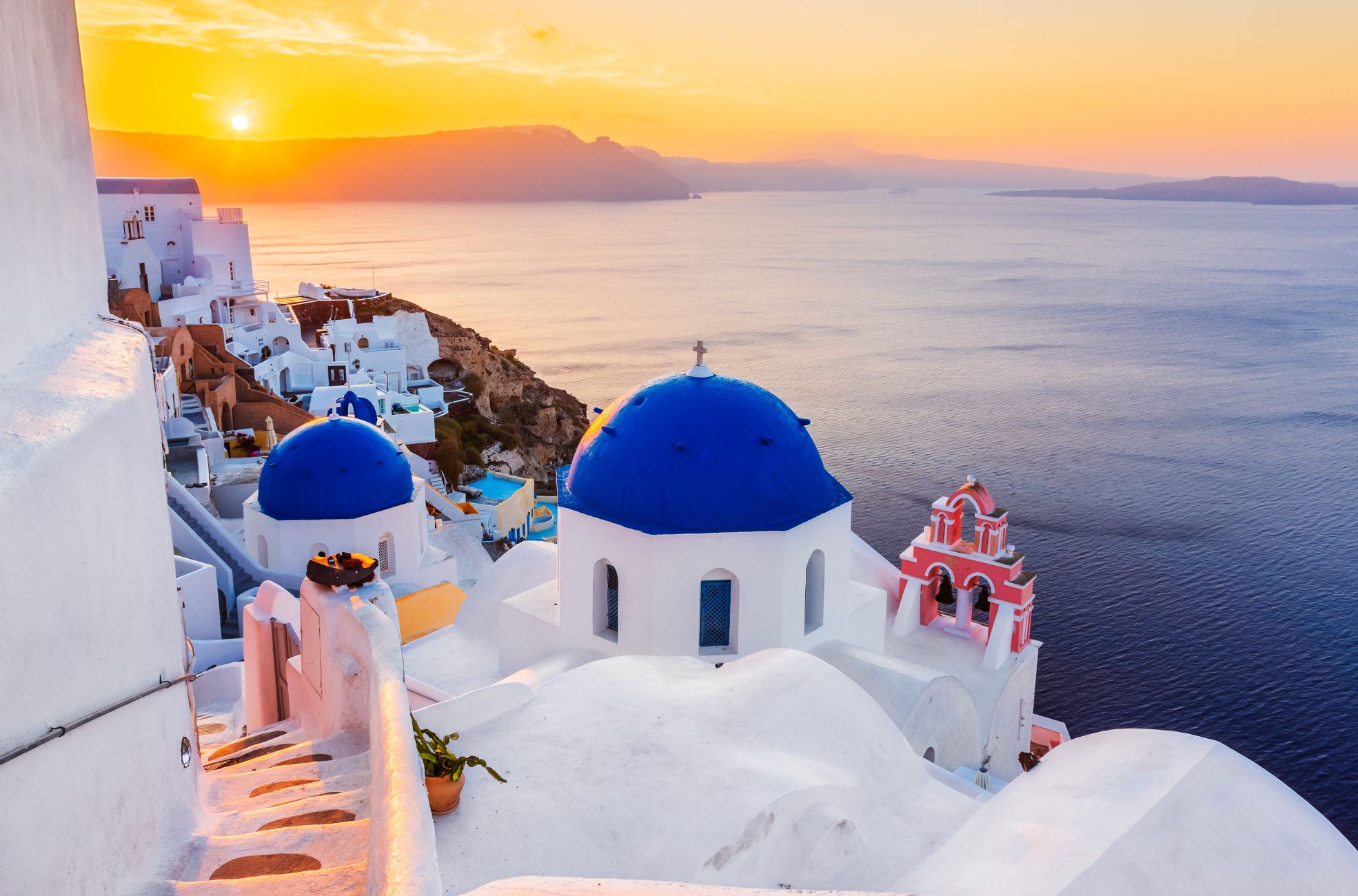 A photo of Greece taken in the late evening, showcasing the beautiful sunset over the mountains and water.