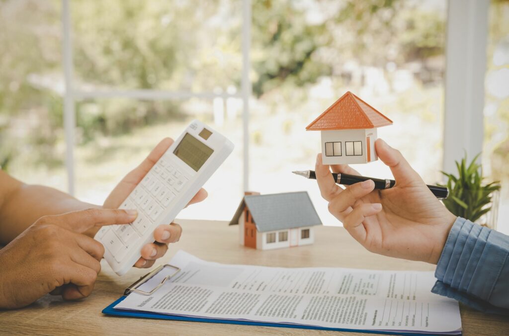 Person Holding Property/House Toy Another Holding Calculator For Buying Cost Estimate
