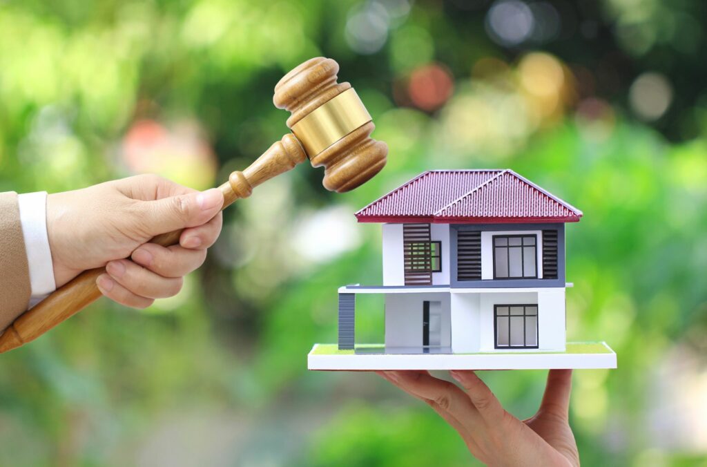 Gavel And Property/House Toy Held In Hands